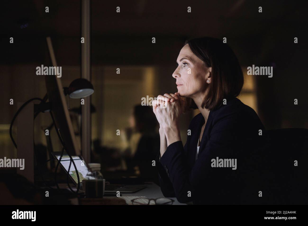 Femme d'affaires mûre avec les mains clastées travaillant sur l'ordinateur dans le bureau la nuit Banque D'Images
