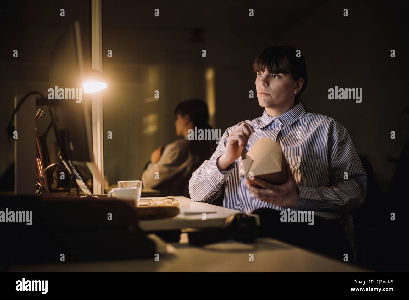 Femme d'affaires avec boîte à nourriture travaillant tard dans le bureau la nuit Banque D'Images