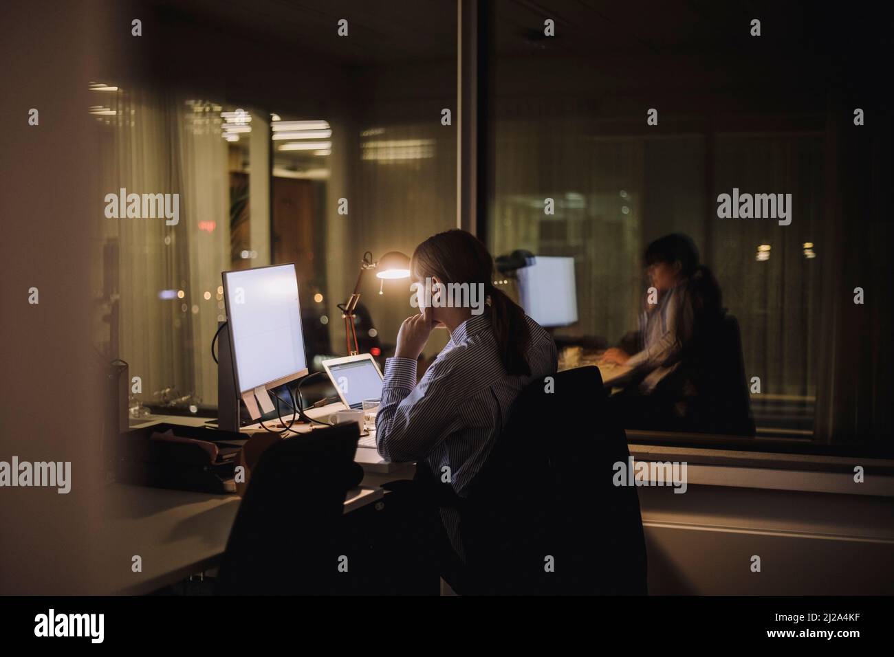 Jeune femme d'affaires travaillant sur ordinateur tard dans la nuit au travail Banque D'Images