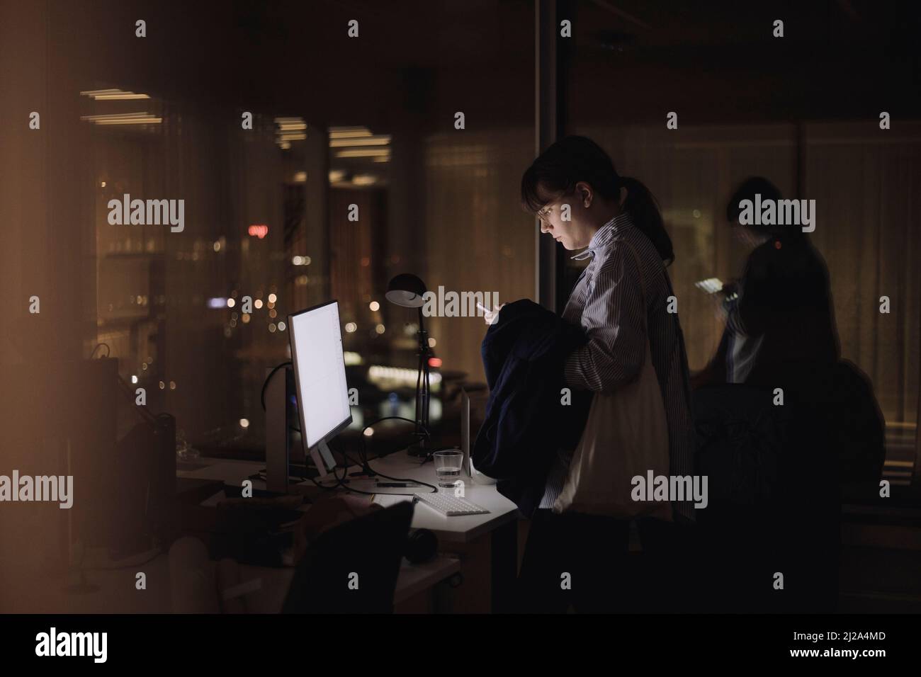 Femme d'affaires utilisant un smartphone tout en travaillant tard dans le bureau la nuit Banque D'Images