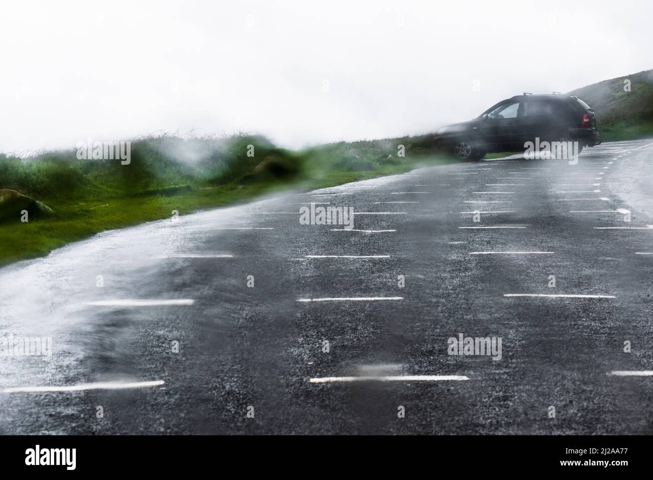 Vue à travers une fenêtre de voiture garée sur la côte lors d'une journée sauvage de gris orage et humide avec une seule autre voiture garée dans le parking. Banque D'Images