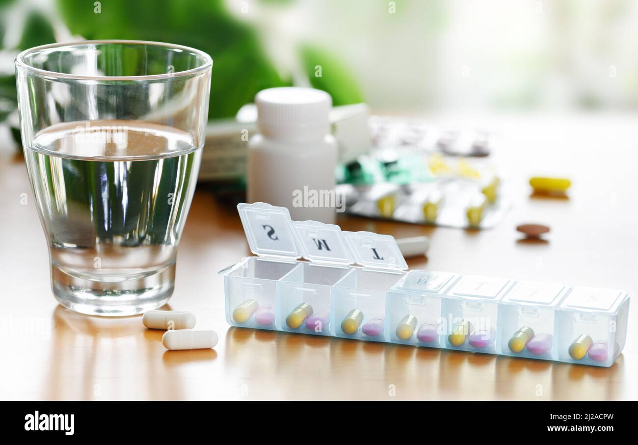 Boîte quotidienne de pilules organiseur de vitamines et de médicaments avec un verre d'eau sur la table. Banque D'Images