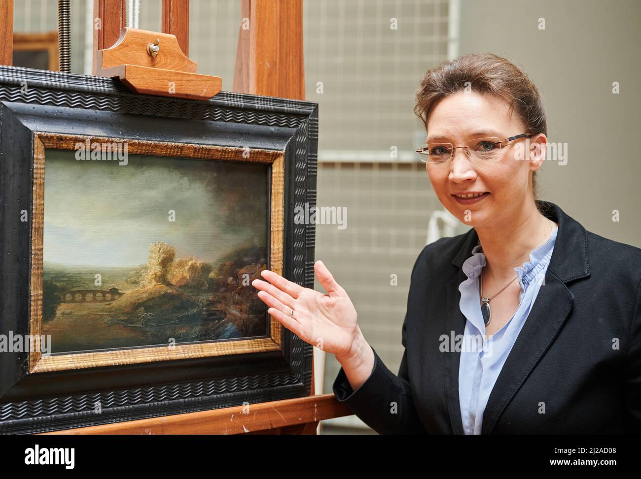 Berlin, Allemagne. 31st mars 2022. Dagmar Hirschfelder, directeur de la Gemäldegalerie, présente la peinture "Paysage avec pont voûté" dans l'atelier de restauration de la Gemäldegalerie. Pendant plus de 30 ans, la peinture 'Paysage avec Pont voûté' a été considérée comme l'œuvre de l'étudiant de Rembrandt, Govert Flinck. Selon les dernières découvertes de la Gemäldegalerie de Berlin, cependant, l'œuvre est par Rembrandt van Rijn (1606-1669) lui-même, à qui elle avait été attribuée plus tôt. Credit: Annette Riedl/dpa/Alay Live News Banque D'Images