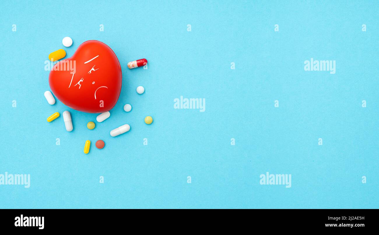 Forme de coeur rouge avec une émotion triste et tas de pilules sur fond bleu, vue de dessus, espace pour le texte, image concept sur la maladie de coeur Banque D'Images