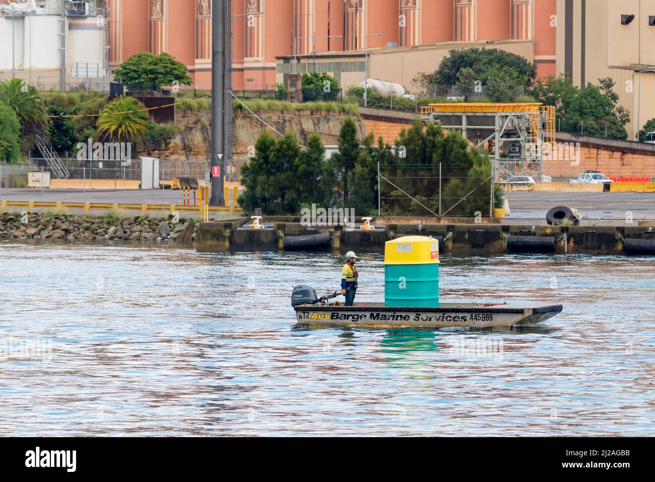 Un homme en tenue haute visibilité et un casque de sécurité, déplaçant une toilette portable dans le port de Sydney en Australie, sur une petite barge commerciale avec un moteur hors-bord Banque D'Images