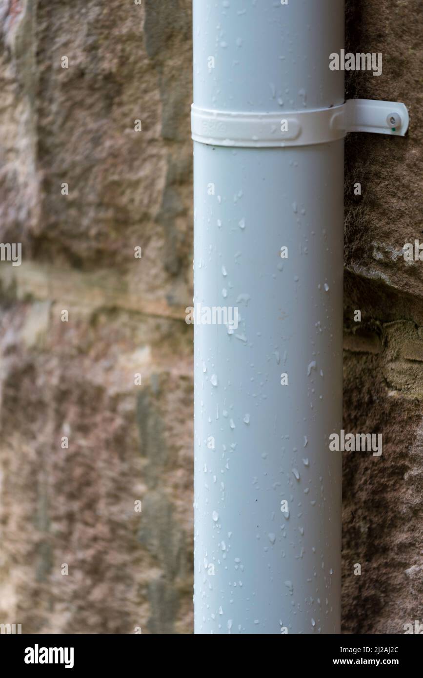 Tuyau de descente en uPVC blanc non plastifié (goulotte) fixé à un mur en grès avec un support en métal poudré Banque D'Images