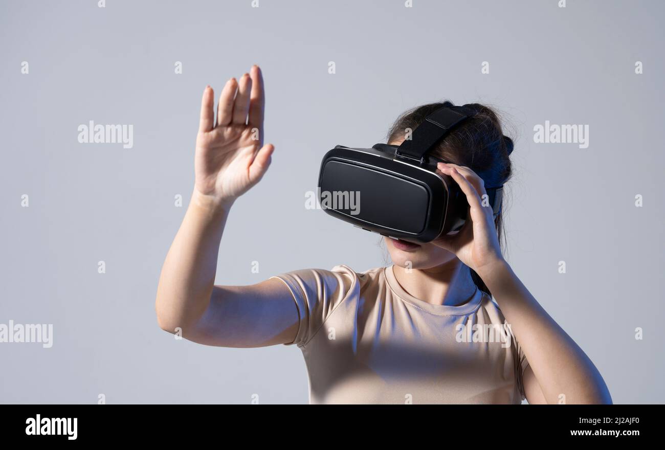 Gros plan de la jeune femme se tient en studio avec des lunettes VR et fait défiler les mains dans l'air.Technologie de réalité virtuelle. Banque D'Images
