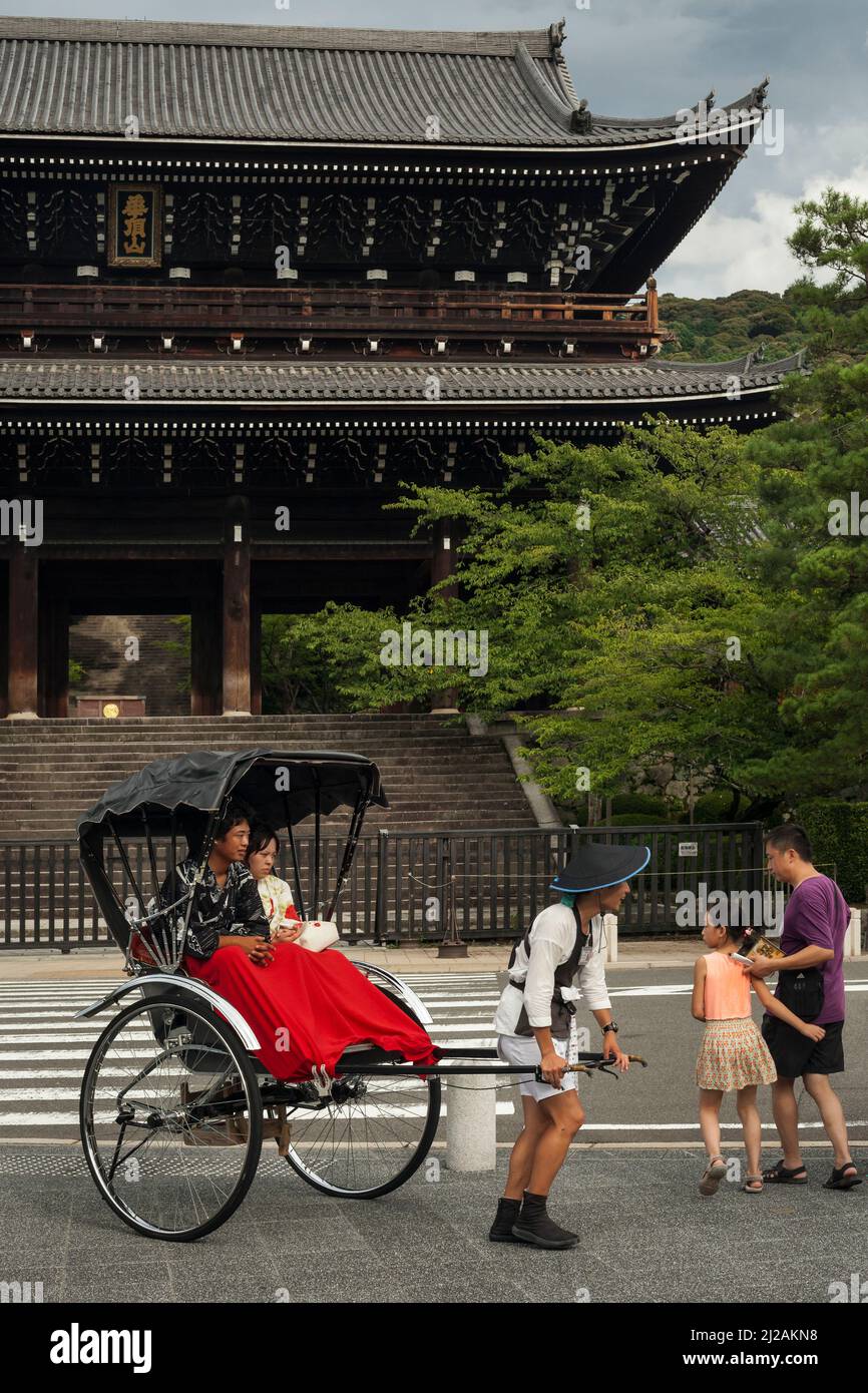 Vue verticale frontale d'un homme habillé de façon traditionnelle portant un pousse-pousse avec quelques touristes devant le temple bouddhiste de Chion-in à Gion, Kyoto Banque D'Images