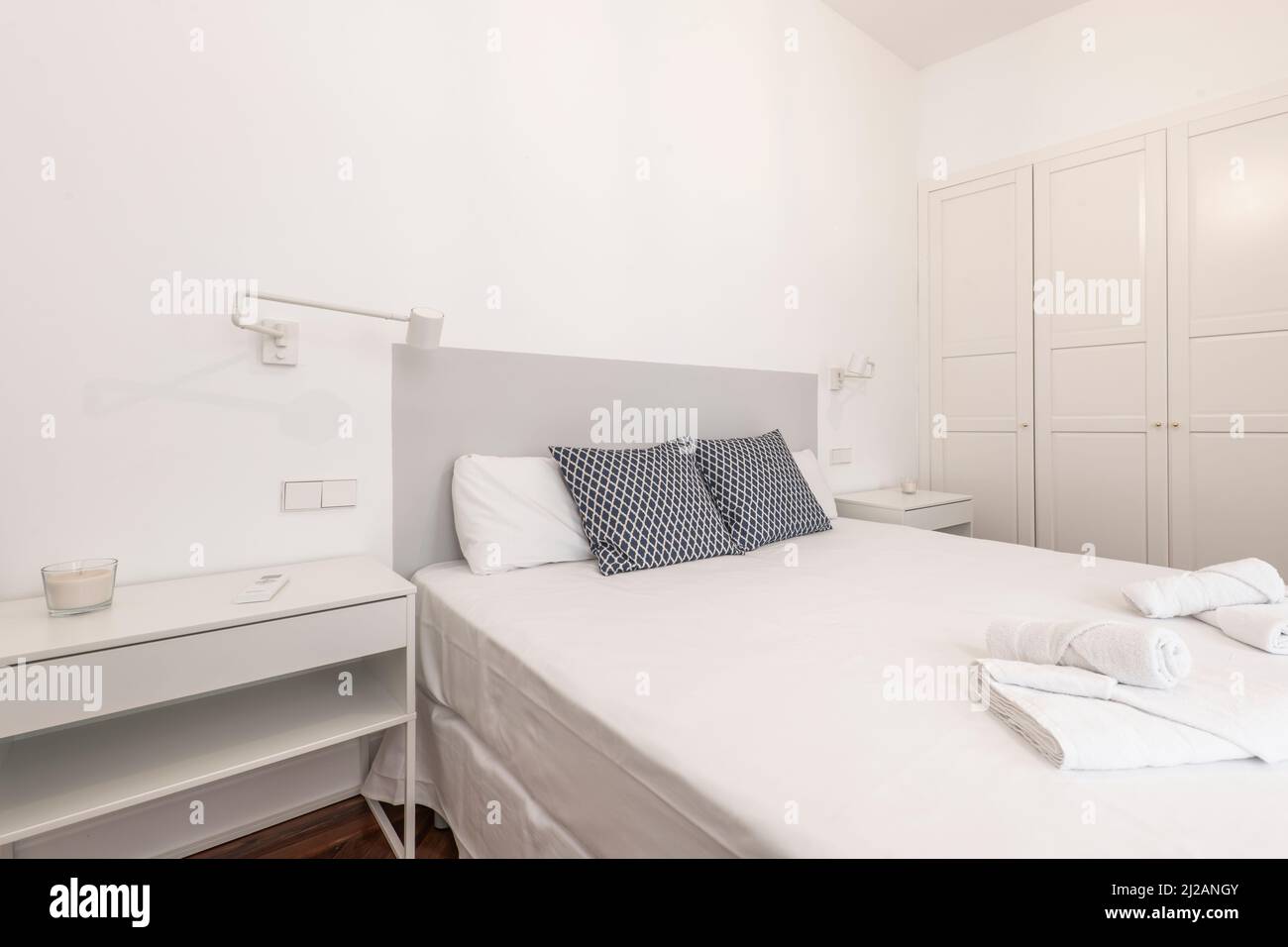 Chambre avec tête de lit en bois gris, armoire en bois blanc intégrée à quatre portes, deux tables de chevet blanches, lampes pliantes, literie et pin à chevrons f Banque D'Images