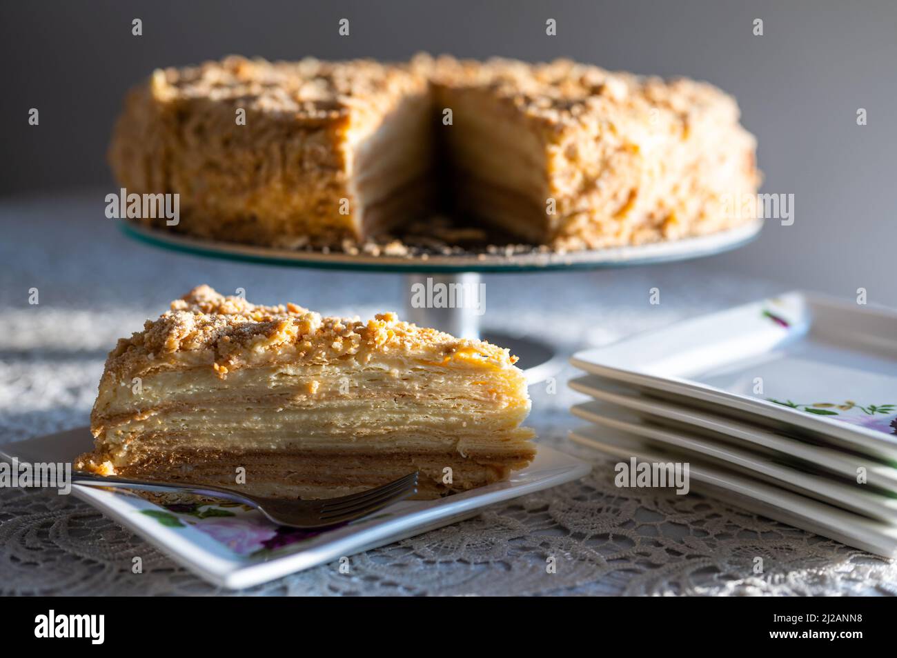 Première tranche de célèbre gâteau Napoléon servi sur une assiette carrée. Tranche de gâteau triangulaire décorée de crumbles croustillantes illuminées par la lumière naturelle du soleil Banque D'Images