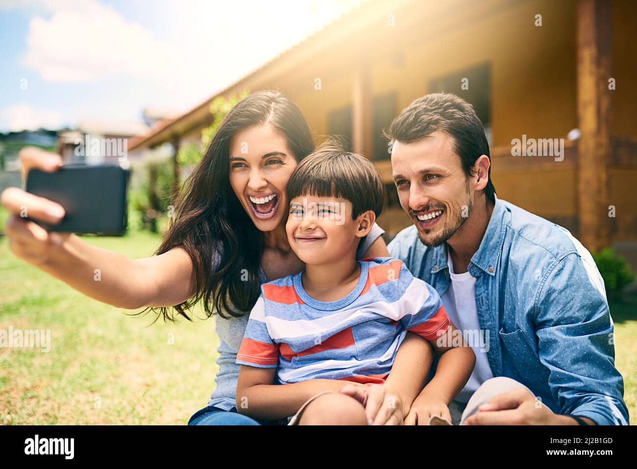 Ceux-ci sont pour l'album photo. Photo courte d'une jeune famille heureuse de trois personnes prenant des selfies blancs assis dans l'arrière-cour. Banque D'Images