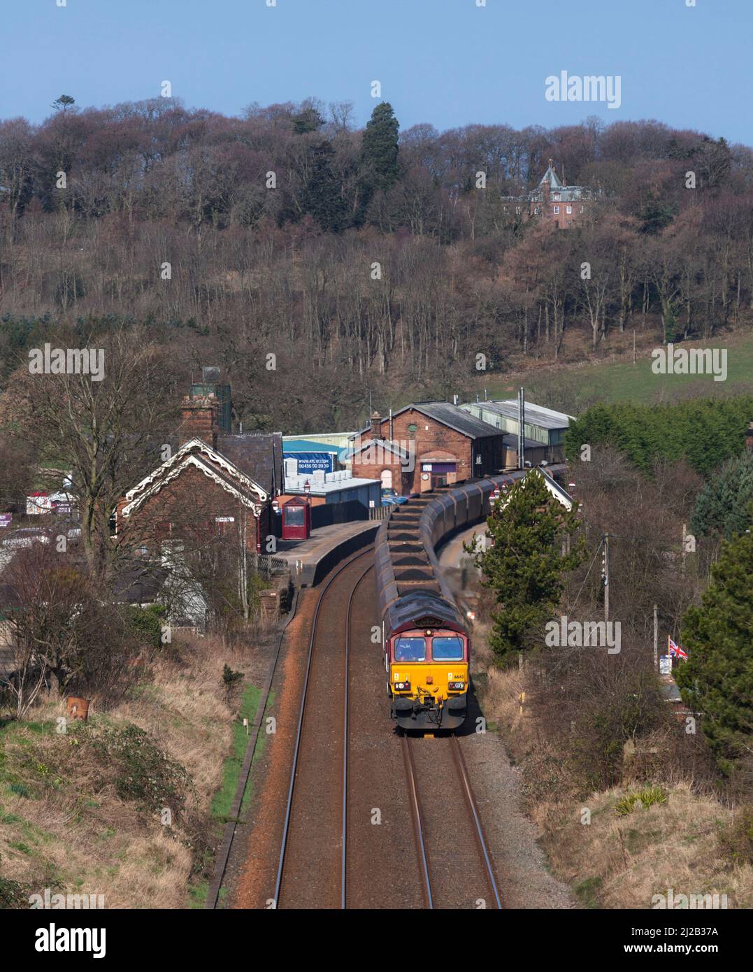DB Schenker classe 66 diesel locomotive 66143 dans la décoration EWS en passant par Lazonby et la gare de Kirkoswald avec un train de charbon rond de merry Go Banque D'Images