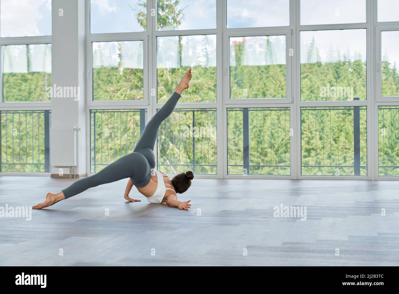 Vue arrière de la jeune femme sportive en forme d'activewear faisant des exercices de fitness dans le hall avec fenêtres panoramiques. Entraînement à l'intérieur avec belle vue sur les montagnes. Banque D'Images