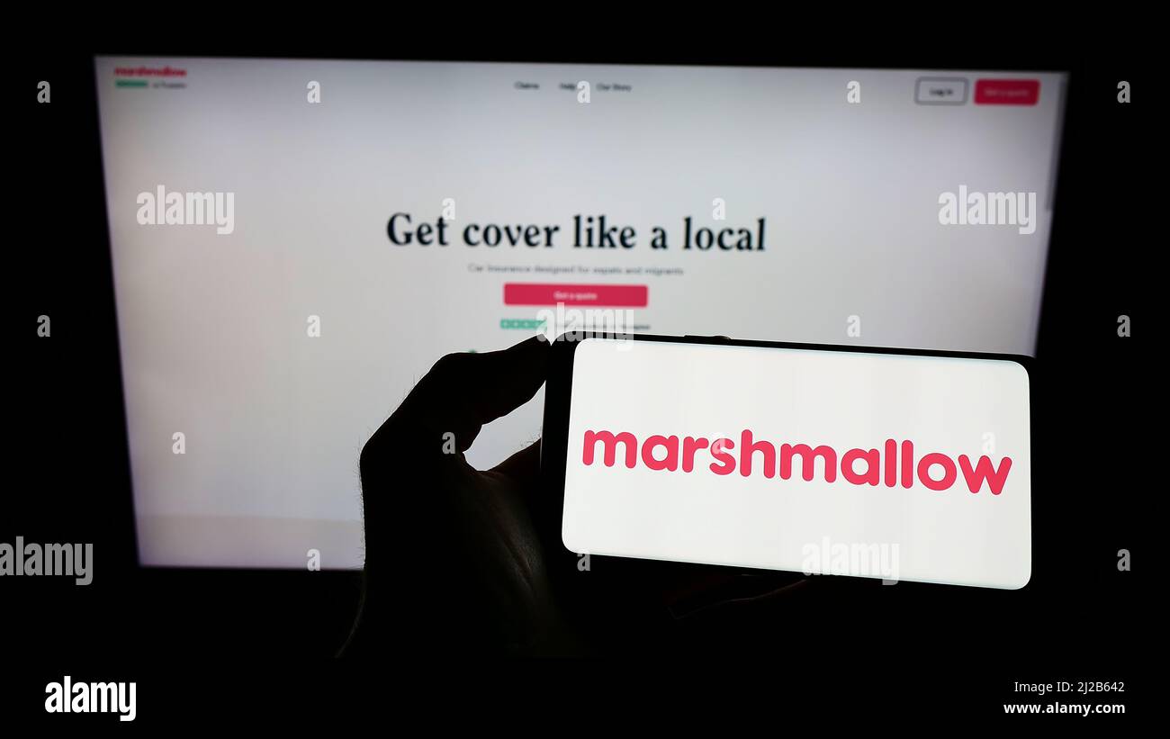 Personne tenant un téléphone cellulaire avec le logo de la société Marshmallow Financial Services Limited à l'écran devant la page Web. Mise au point sur l'affichage du téléphone. Banque D'Images