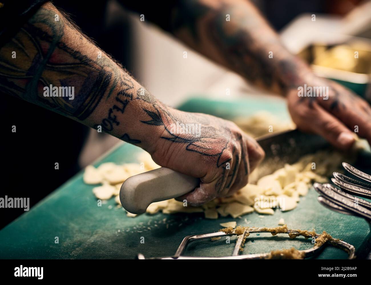 Une image nette. Gros plan d'un chef méconnu tatoué les mains coupant des légumes avec un couteau sur une planche dans une cuisine. Banque D'Images