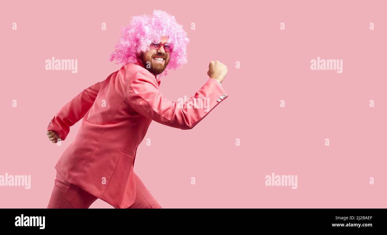 Clown drôle en rose perruque, costume et lunettes de soleil courant isolé sur fond de couleur rose Banque D'Images