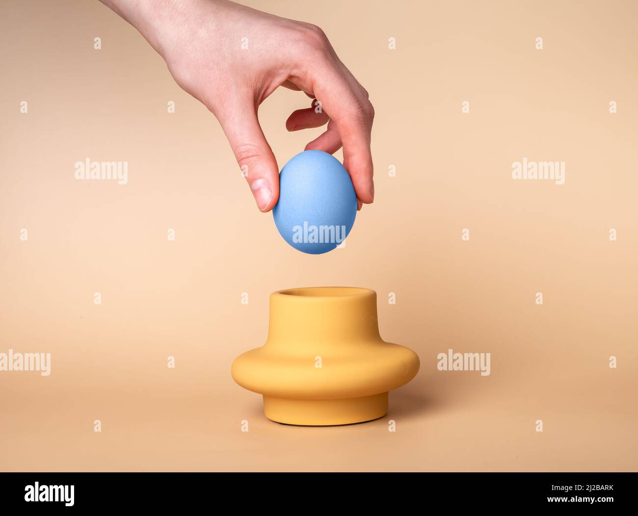 Faire passer à la main l'œuf bleu teint dans la tasse. Support et serveur sur fond beige. Concept de tradition de célébration de Pâques. Photo de haute qualité Banque D'Images