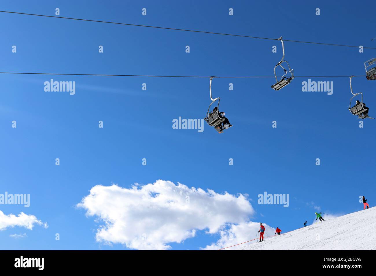 Une image générique d'un télésiège avec des skieurs au loin, dans un paysage enneigé, vu contre un ciel bleu vif et des nuages blancs moelleux (Autriche) Banque D'Images