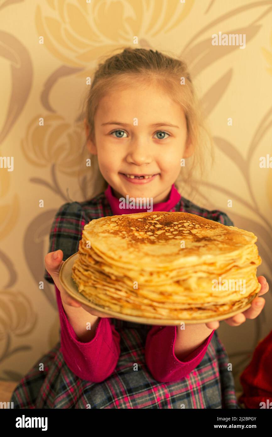 Une fille tient une assiette avec une pile de crêpes. Banque D'Images