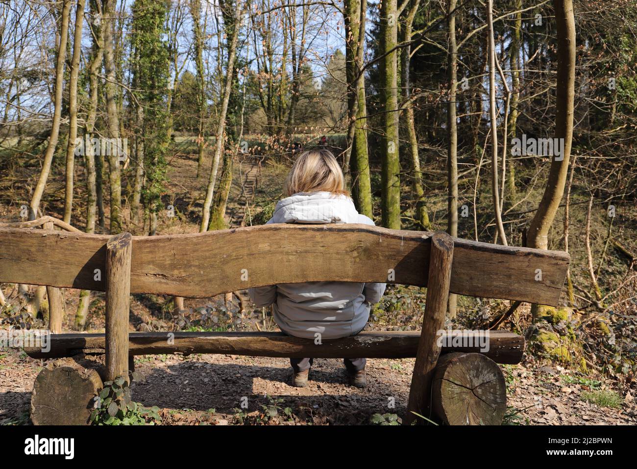 une femme blonde est assise avec une veste sur un banc dans la forêt Banque D'Images