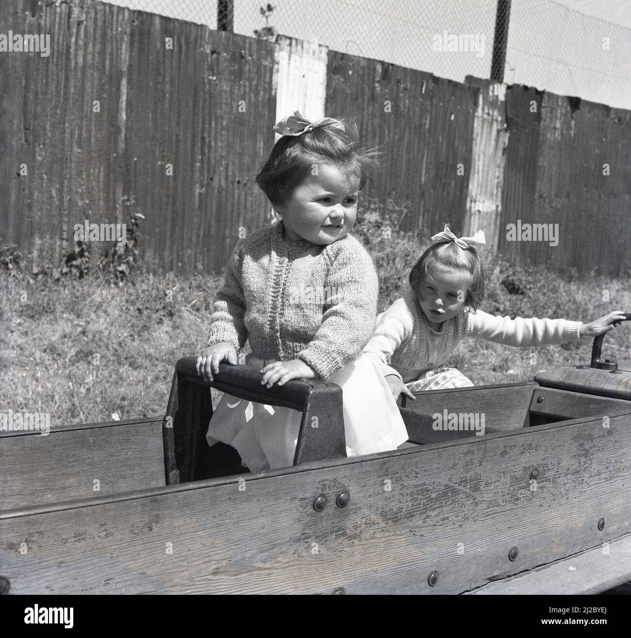 1961, à l'extérieur dans un terrain de jeu, deux petites filles assises dans un cheval à bascule encadré de bois, Angleterre, Royaume-Uni. Le premier terrain de jeu au monde remonte à la mi-1800s, où un espace a été créé pour les enfants à jouer avec des blocs de bois et des jouets. Le terrain de jeu tel que nous l'avons connu aujourd'hui, développé comme un moyen d'encourager les enfants hors de la rue et à partir de 1930s, en bois et en métal structures, telles que les toboggans, balançoires, cadres d'escalade et manèges, a fourni un point de vente pour les enfants de s'amuser dehors. L'introduction de nouvelles réglementations en matière de santé et de sécurité a vu de telles structures retirées du 1980s. Banque D'Images