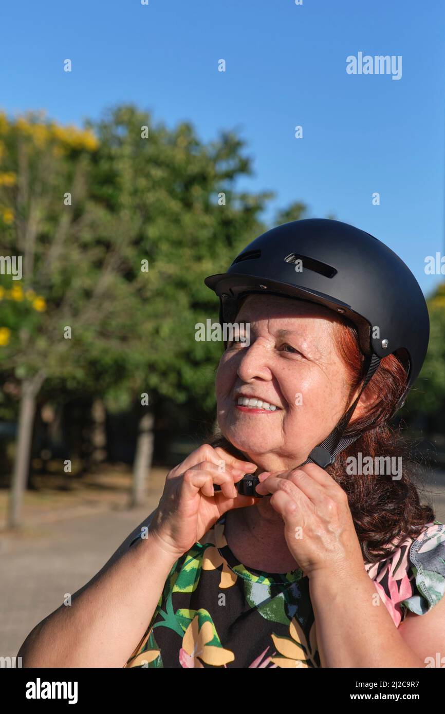 Heureuse femme hispanique mûre souriante portant un casque de sport dans un parc municipal. Concepts de vie urbaine active, de bien-être et de sécurité routière. Banque D'Images