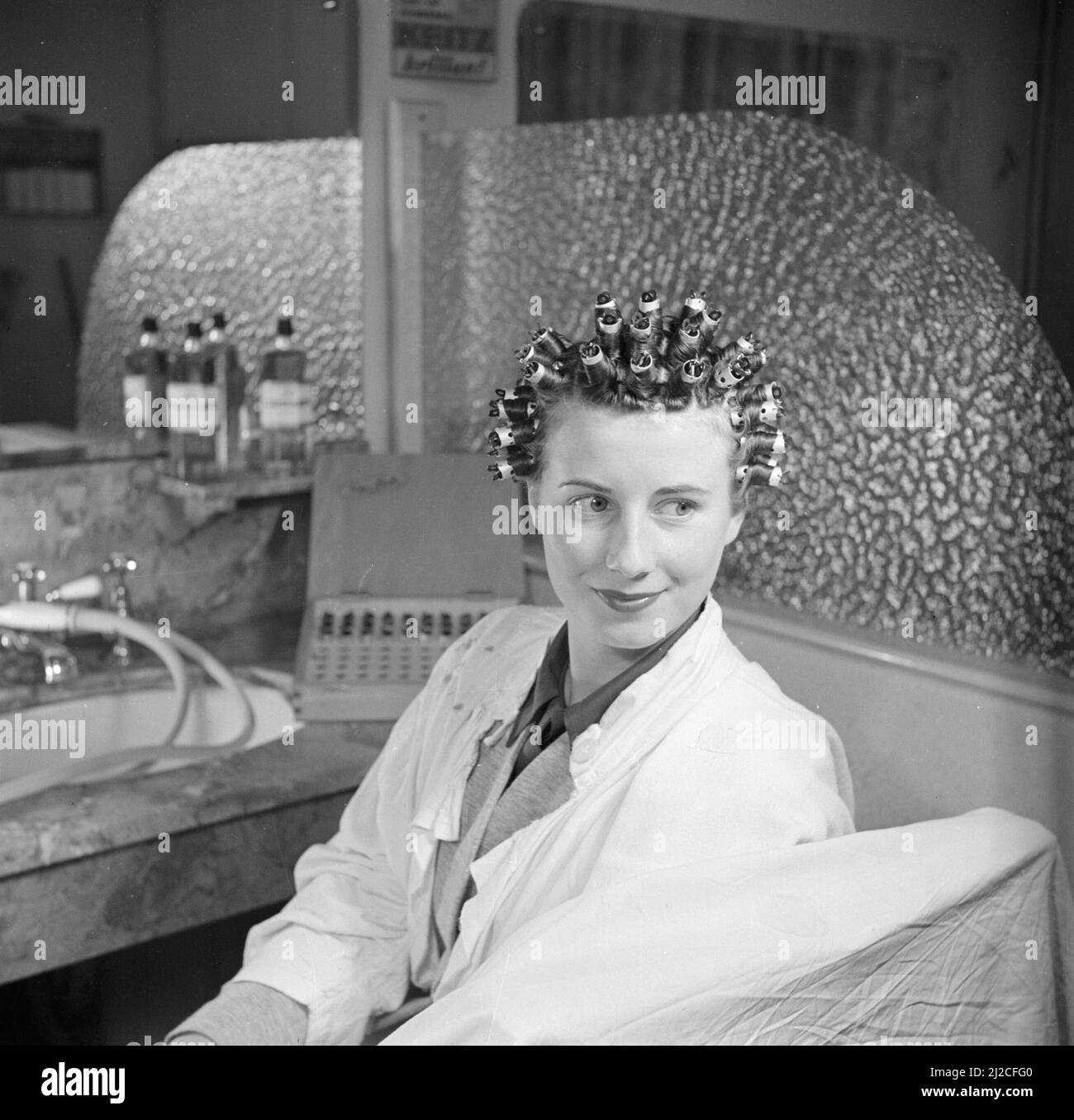 Femme assise dans une chaise dans un salon de coiffure ou salon de beauté ca. 1950 Banque D'Images