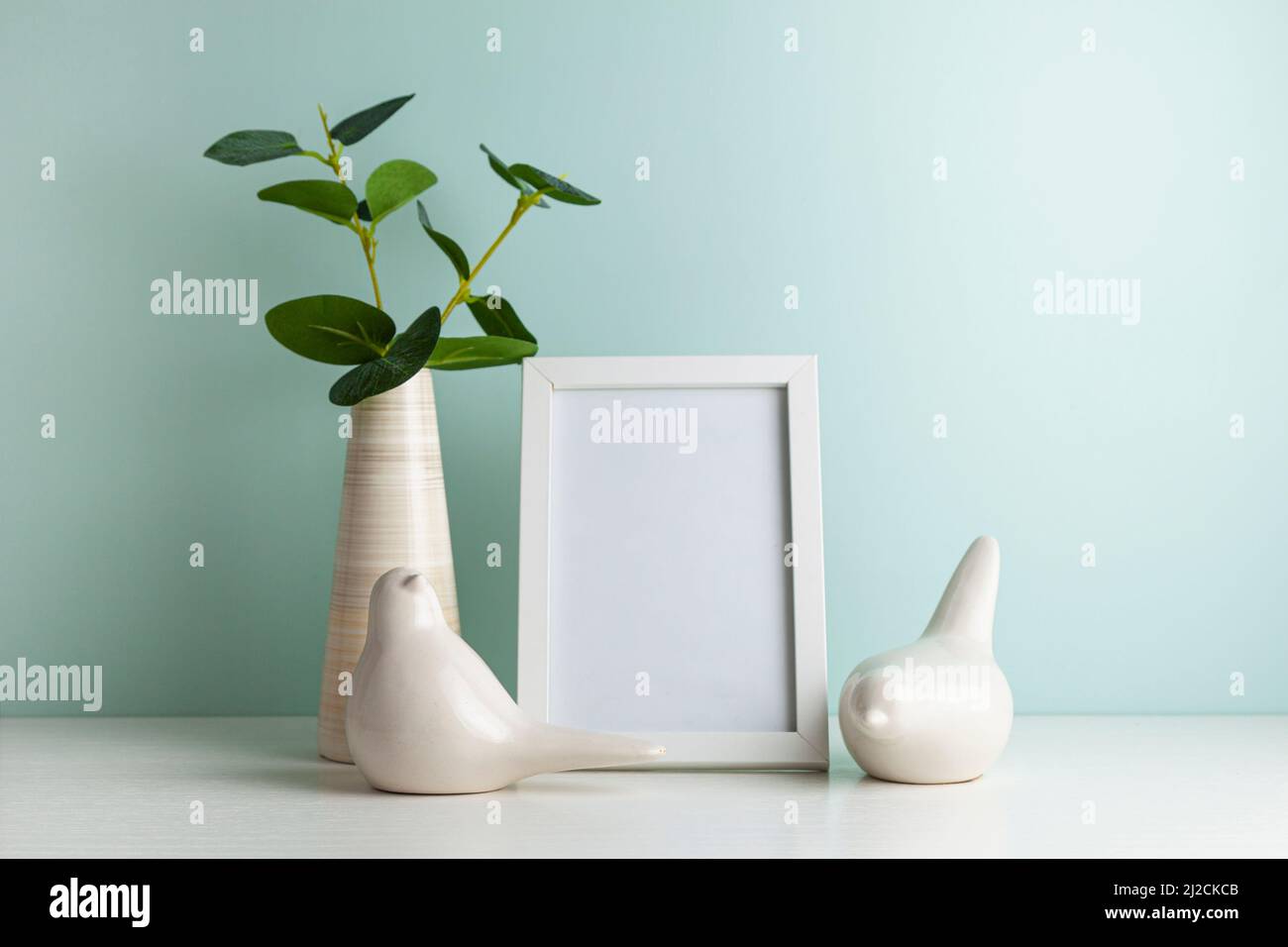 Table de bureau confortable avec vase avec branche verte, oiseau en céramique et cadre photo. Hygge, style boho, salon scandinave. Banque D'Images