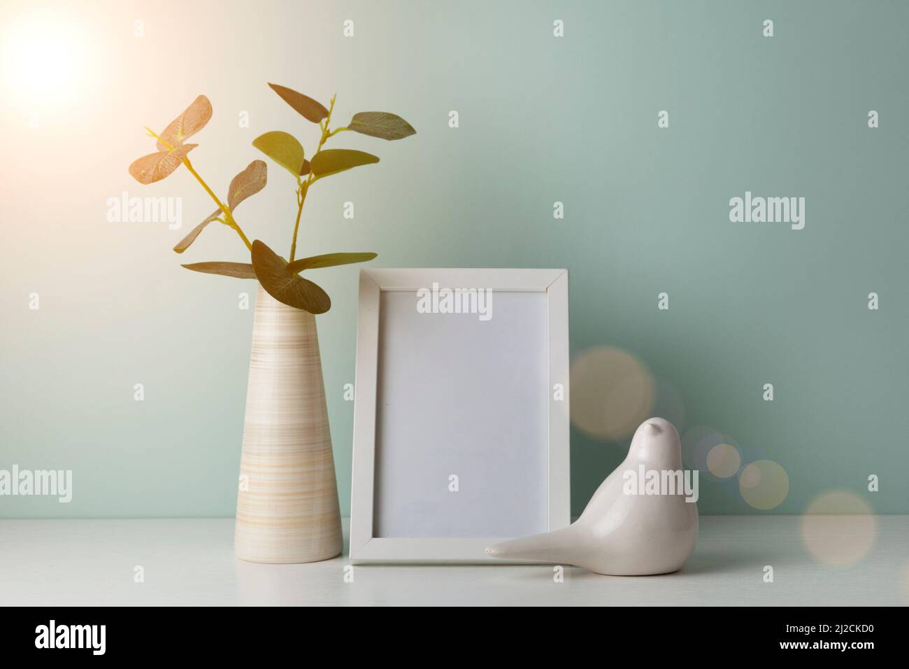 Table de bureau confortable avec vase avec branche verte, oiseau en céramique et cadre photo. Hygge, style boho, salon scandinave Banque D'Images