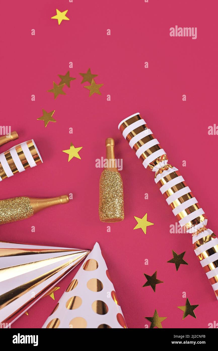 Chapeaux de fête, petites bouteilles de champagne dorées, confettis d'étoiles et cadeaux sur fond rose Banque D'Images