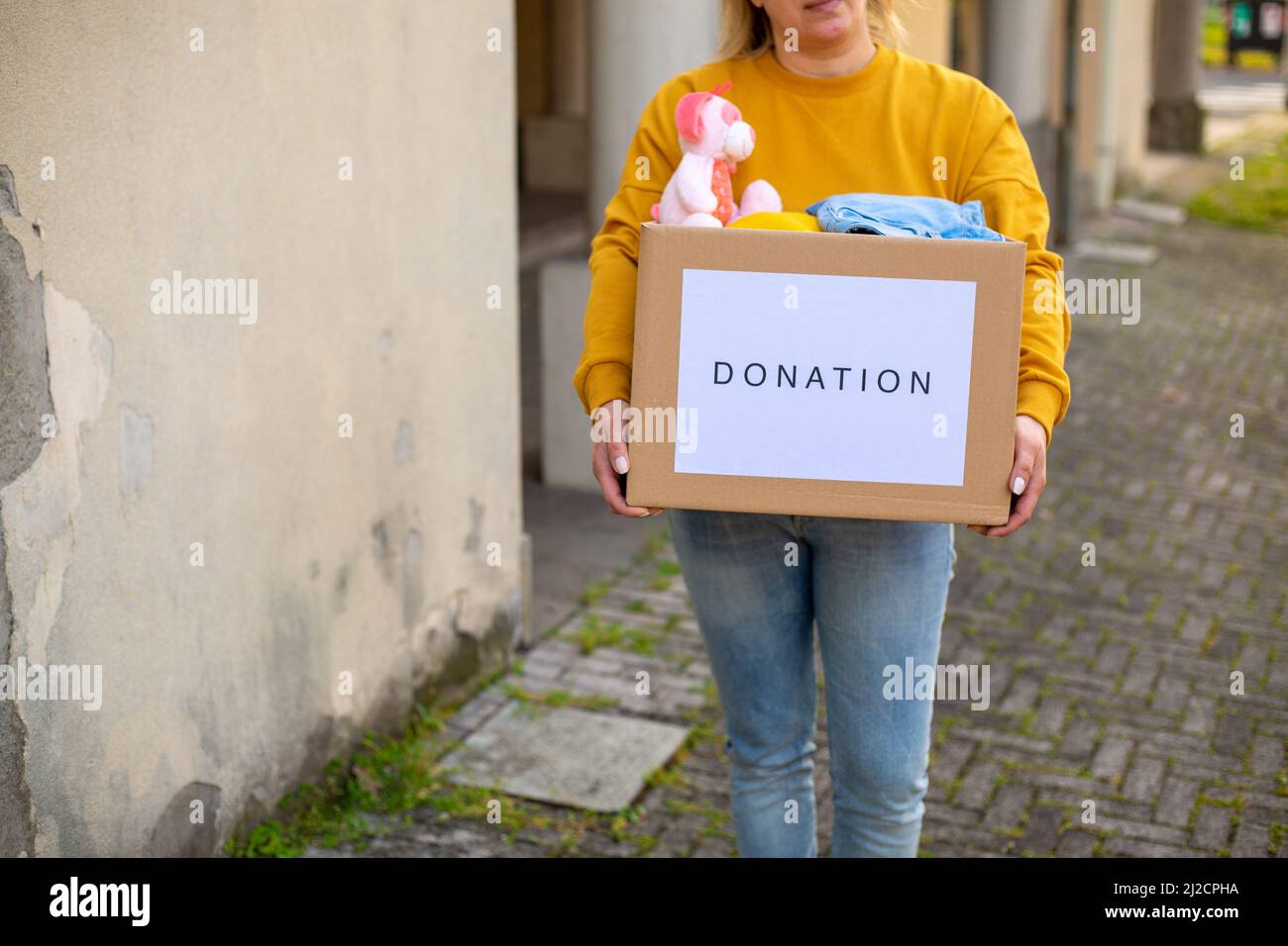 Une volontaire femelle tient une boîte d'aide humanitaire avec des choses et des jouets pour enfants pour les besoins des Ukrainiens dans la rue. Aide pour l'Ukraine Banque D'Images