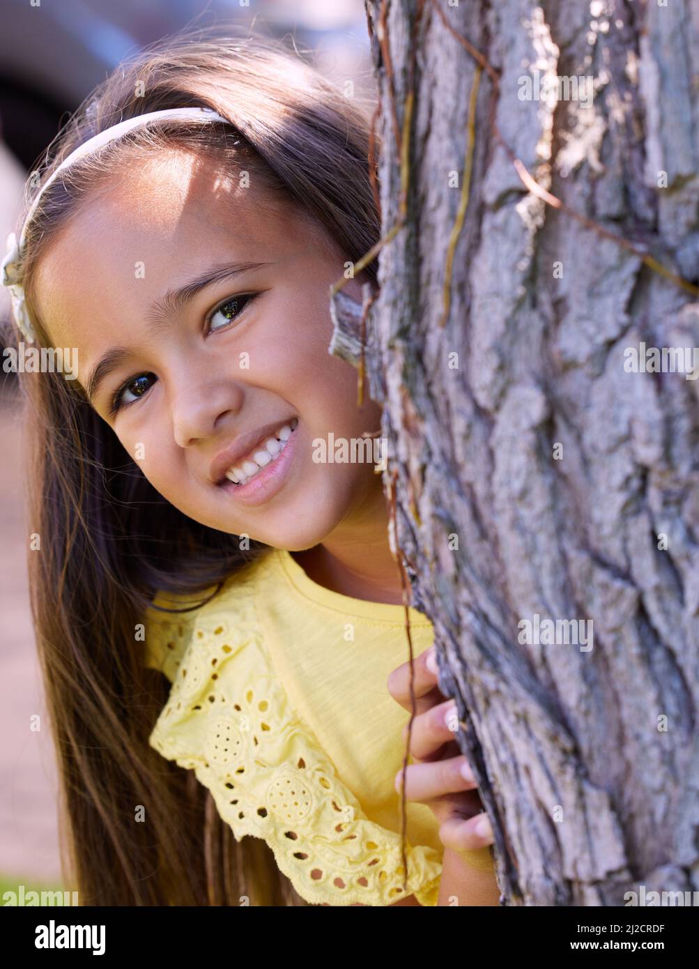 Ne parlez à personne de mon endroit préféré où se cacher et chercher. Photo d'une adorable petite fille qui se cache derrière un arbre. Banque D'Images