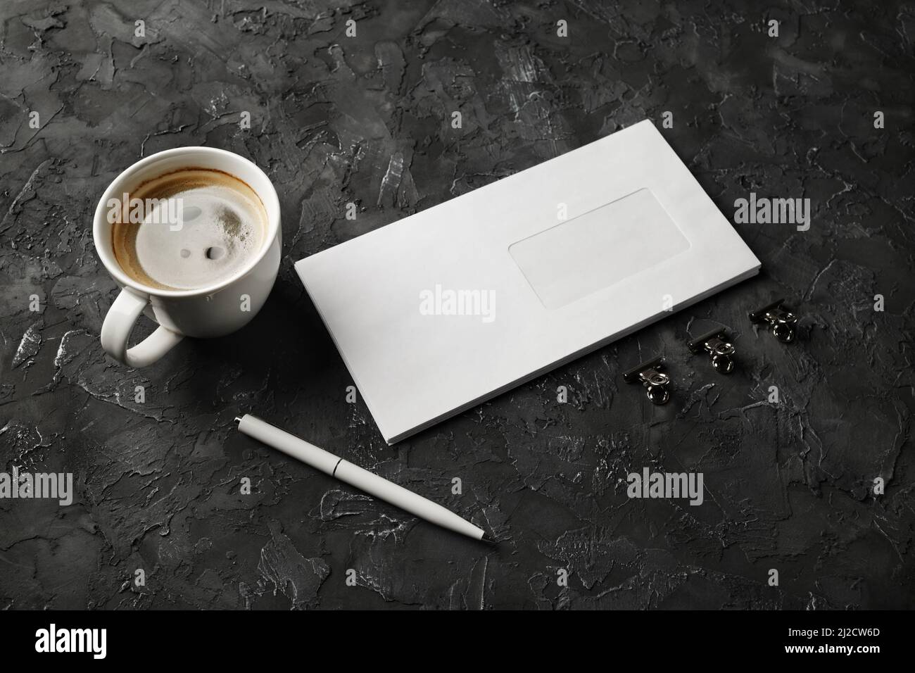 Enveloppe vierge, tasse à café, stylo et pinces sur fond de plâtre noir. Maquette de marque. Banque D'Images