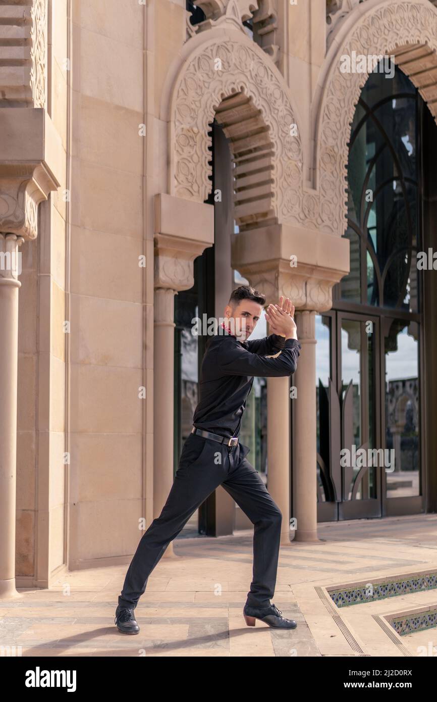Danseur espagnol de flamenco vêtu de noir posant et se claquant les mains devant une arche de style mudéjar Banque D'Images