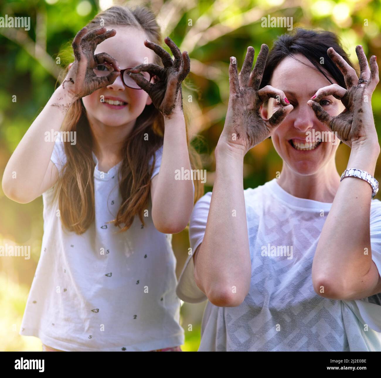 Jouez ensemble. Restez ensemble. Portrait d'une mère et de sa petite fille couvrant leurs yeux avec leurs mains boueuses dehors. Banque D'Images