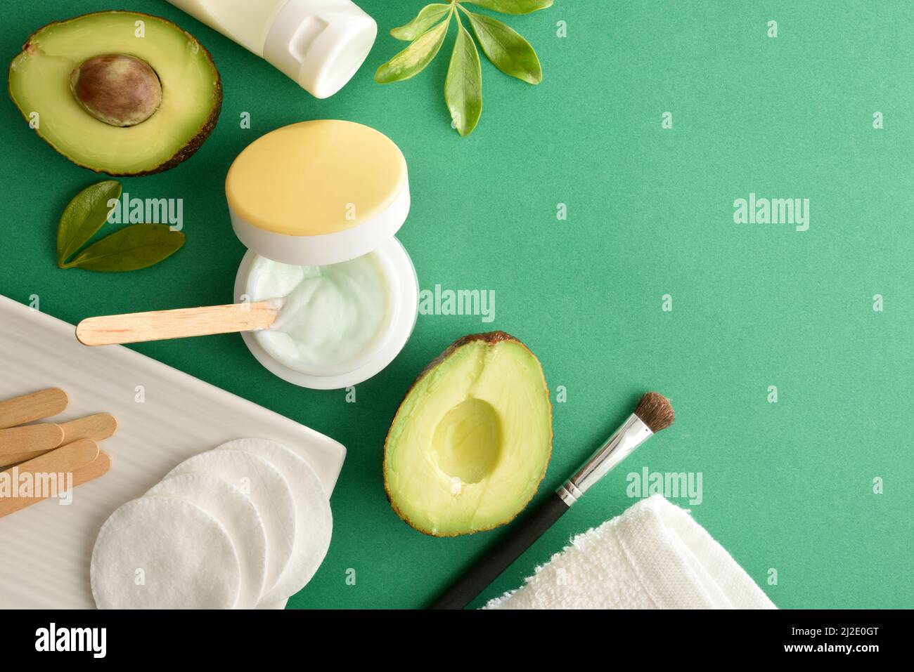 Crème hydratante et lotion à l'extrait d'avocat pour les soins de la peau avec des produits de toilette sur table verte. Vue de dessus. Composition horizontale. Banque D'Images