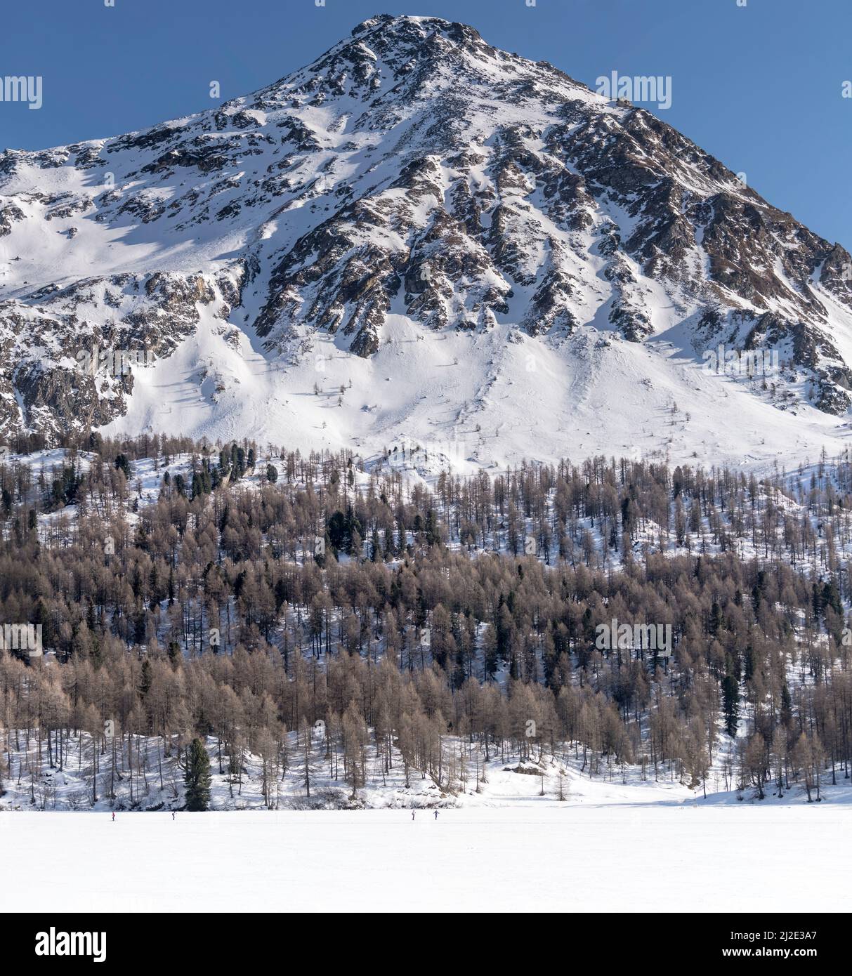 Paysage d'hiver avec les skieurs de fond sur lac gelé avec chaîne de montagne en arrière-plan , tourné en lumière vive près de Maloja, Grisons, Suisse Banque D'Images