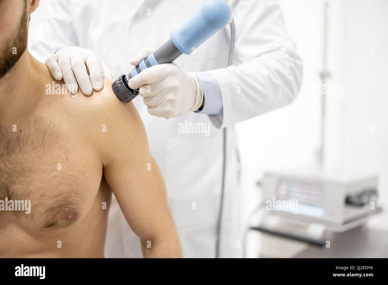 Le médecin applique un traitement par onde de choc sur l'épaule des hommes Banque D'Images