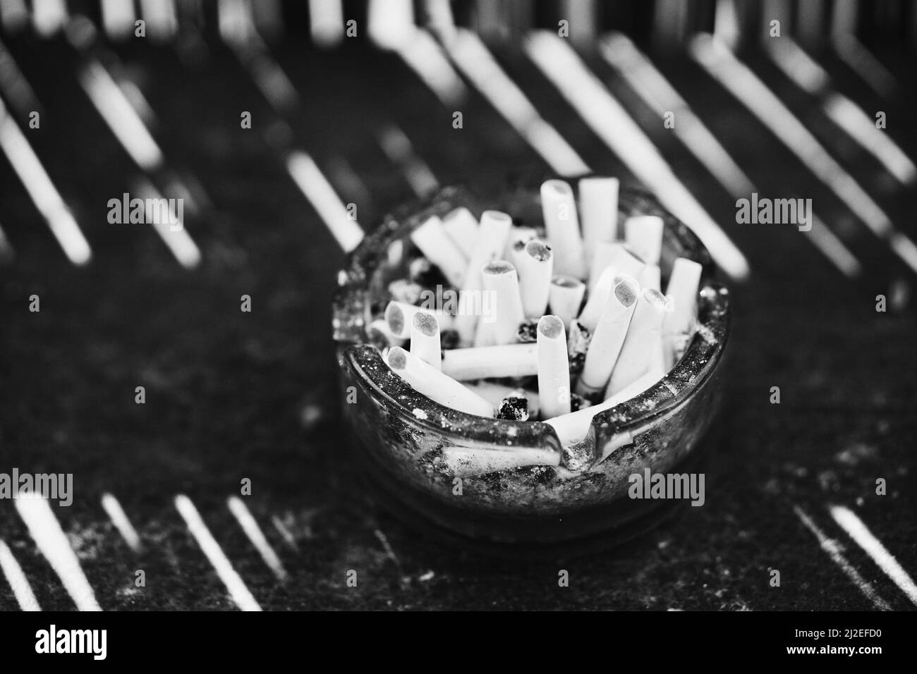 Gros plan de cigarettes fumées sur un cendrier transparent en niveaux de gris Banque D'Images