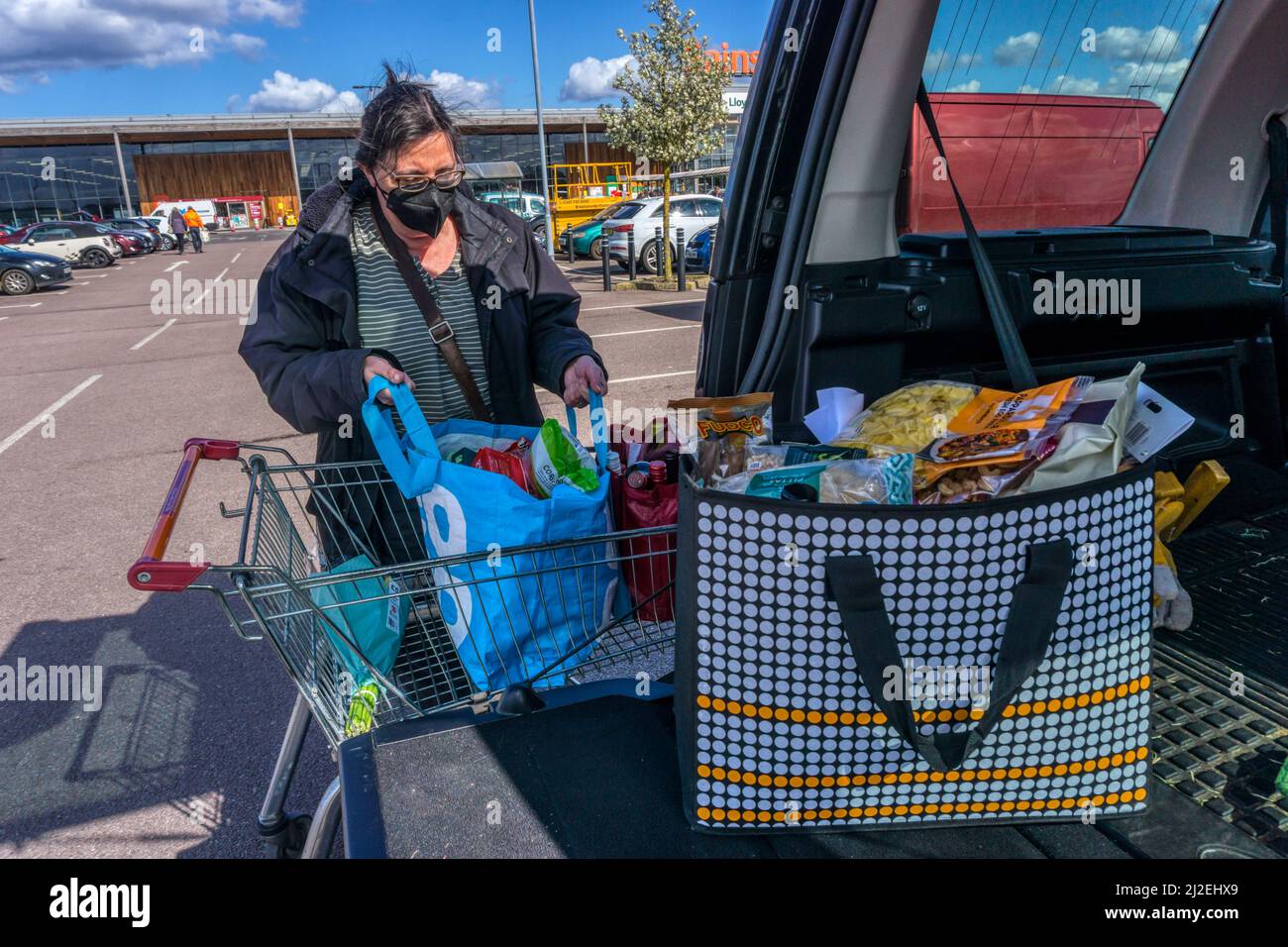 Femme déchargeant sa boutique hebdomadaire du tramway dans un parking de supermarché à l'arrière de sa voiture. NB : version du modèle disponible pour les personnes en premier plan Banque D'Images