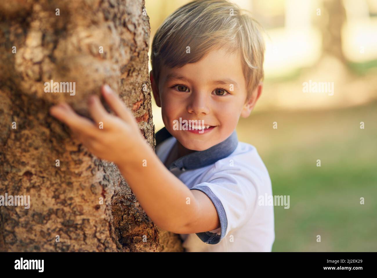 Masquer et rechercher un expert de niveau. Photo d'un petit garçon heureux jouant à côté d'un arbre dans le parc. Banque D'Images