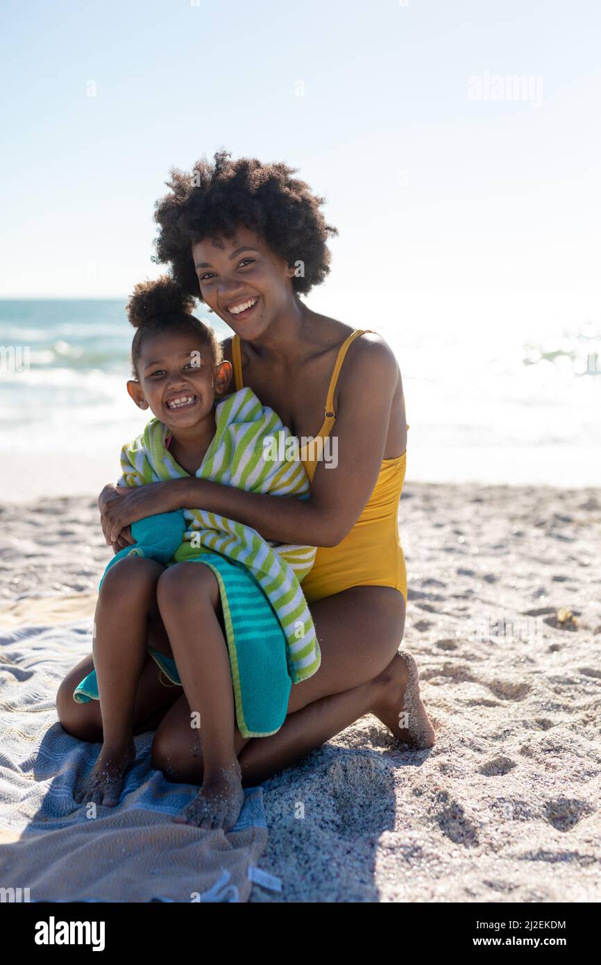 Portrait d'une mère et d'une fille afro-américaines heureuses assises sur le sable à la plage pendant la journée ensoleillée Banque D'Images