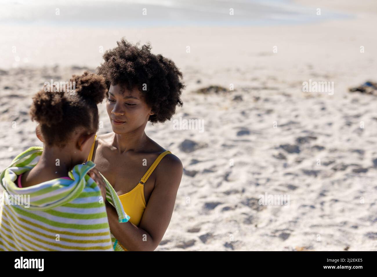 Femme afro-américaine enveloppant sa fille d'une serviette le jour ensoleillé à la plage Banque D'Images