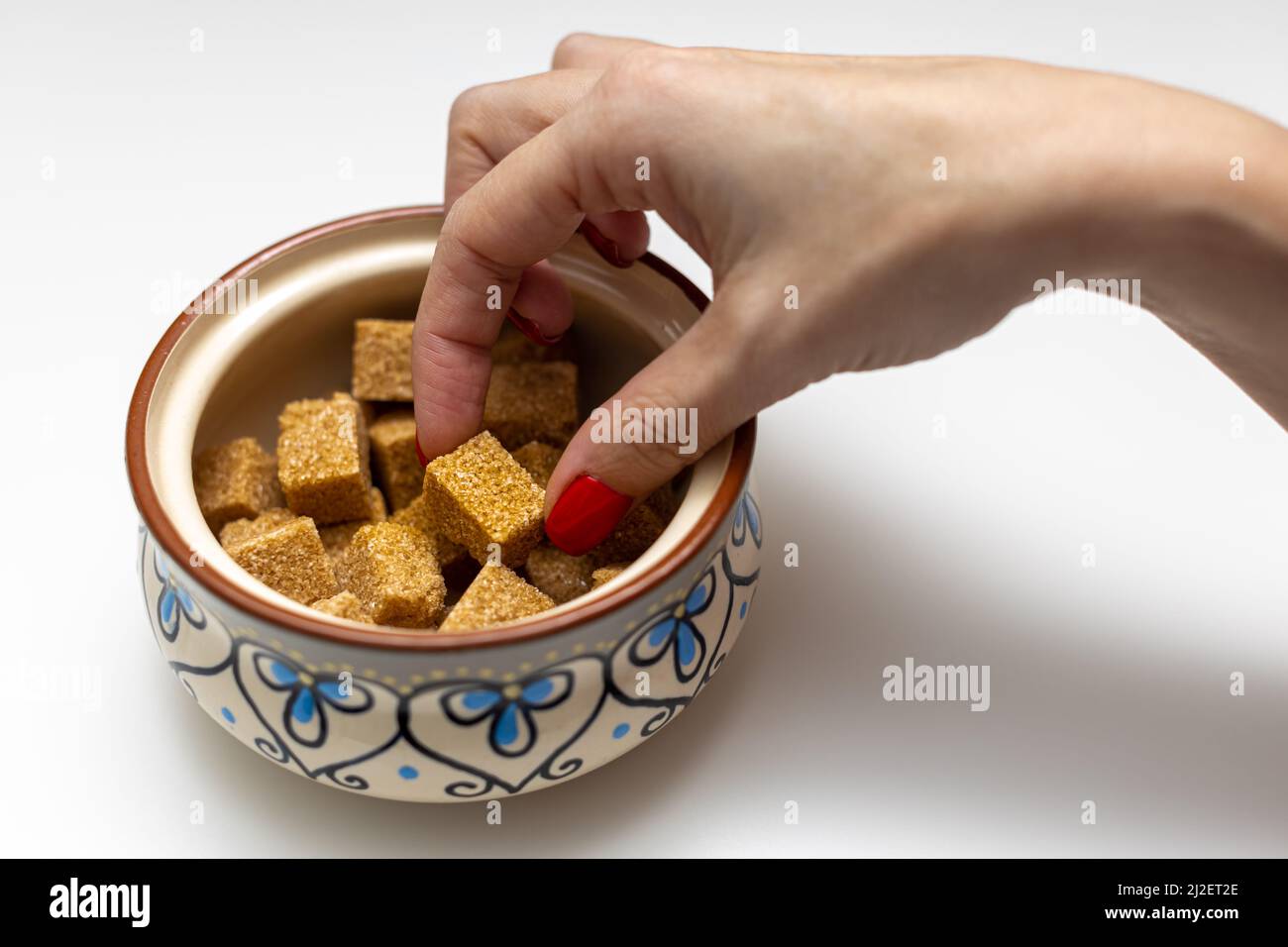 la main d'une femme sort un cube de sucre brun d'un bol à sucre. Photo de haute qualité Banque D'Images