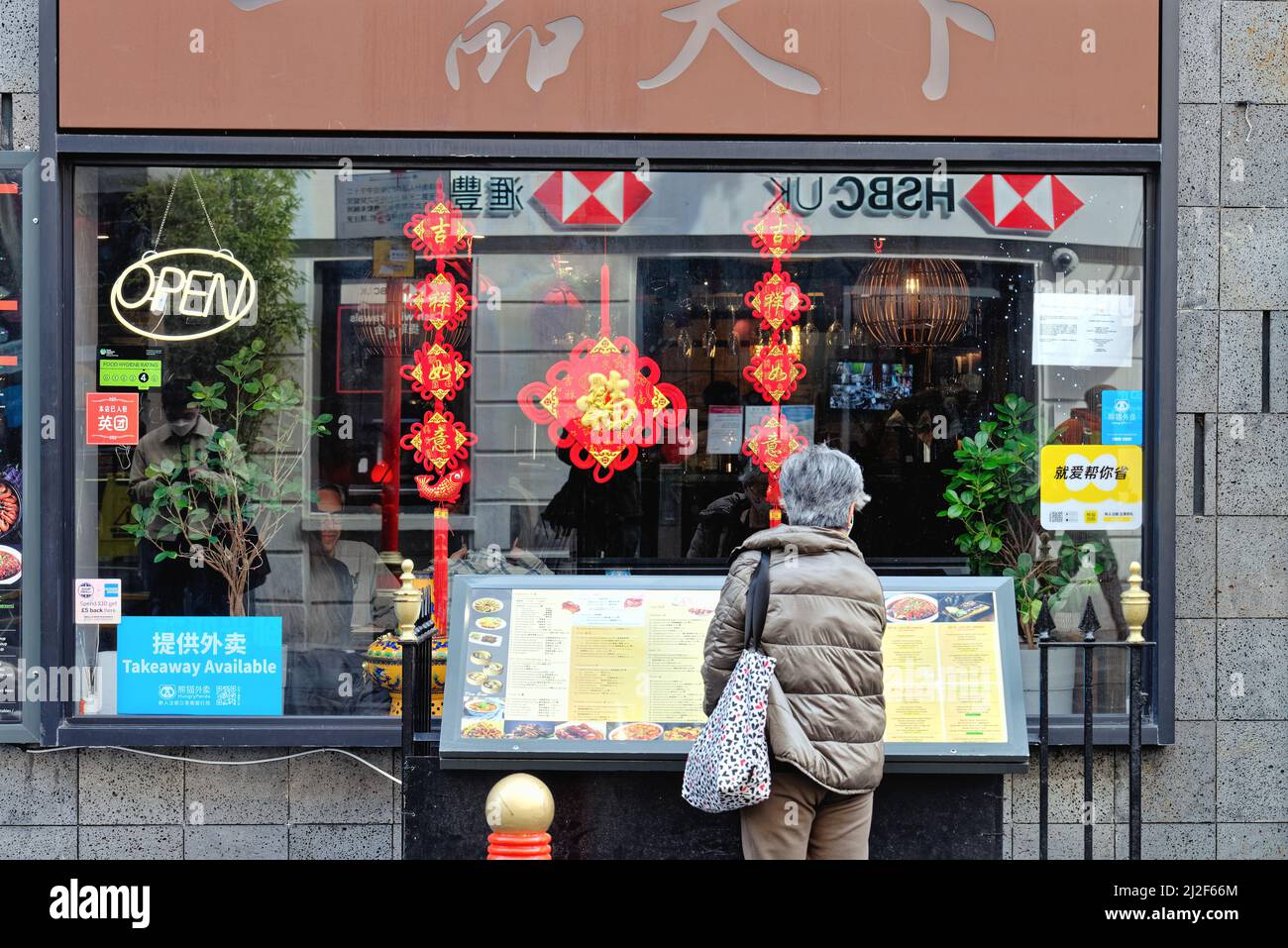 Vue arrière d'une femme mûre aux cheveux gris qui regarde un menu à l'extérieur d'un restaurant chinois sur Gerrard Street Chinatown Central London England UK Banque D'Images