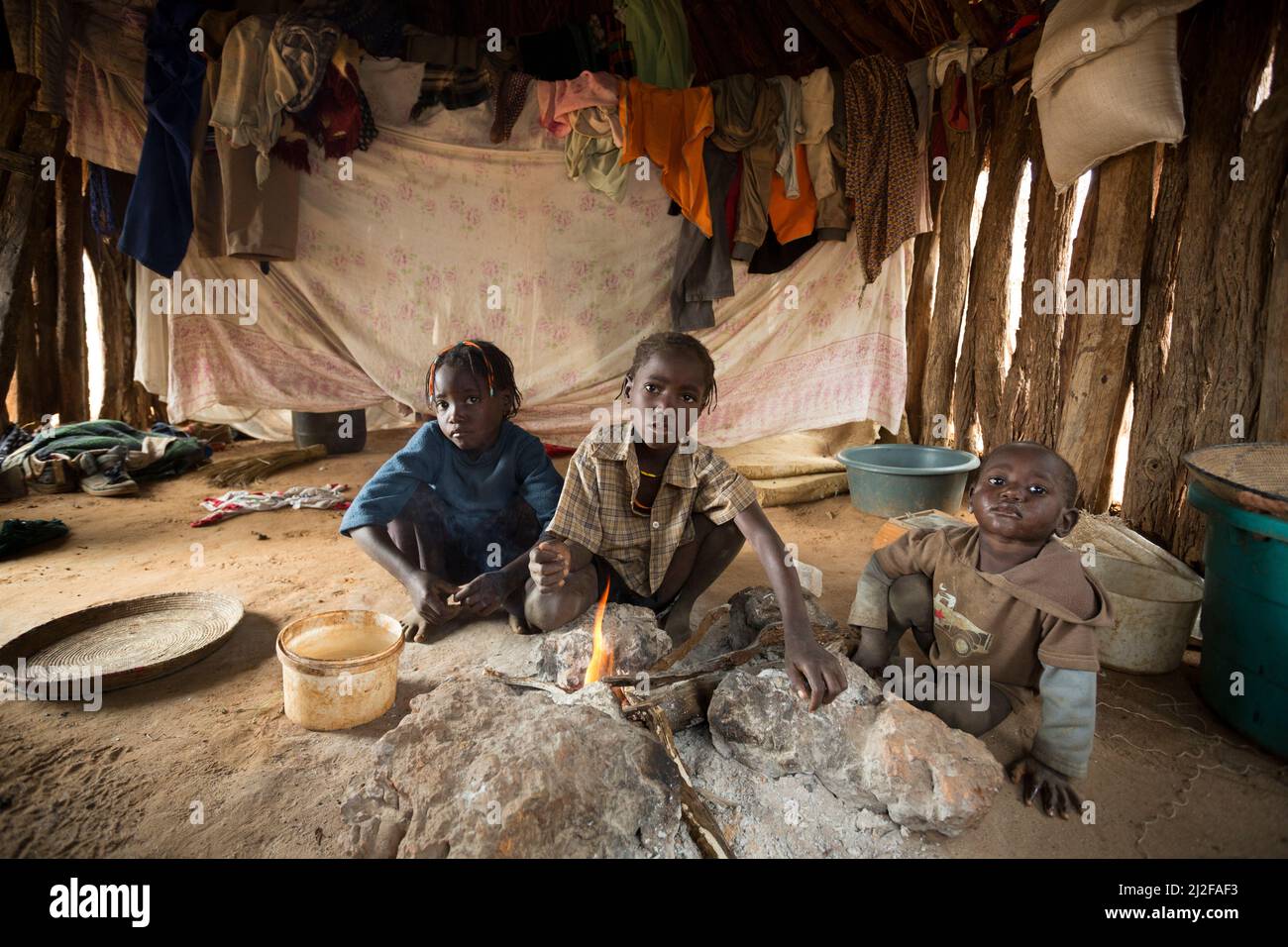 Trois enfants se réchauffent par le feu dans leur cabane à une pièce dans la région d'Omusati, en Namibie, en Afrique du Sud-Ouest. Banque D'Images