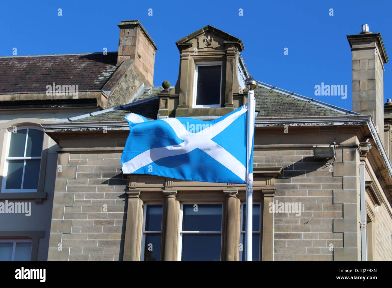 Drapeau de l'Écosse, également connu sous le nom de St Andrew's Cross ou The Saltyre, volant dans le vent le jour d'été ensoleillé (High Street, Peebles, Écosse) Banque D'Images