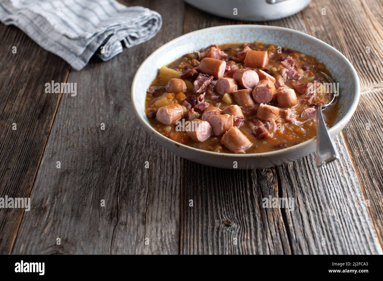 Ragoût de porc viande maison avec légumes, pommes de terre, haricots et saucisse bouillie. Servi dans un bol avec une cuillère sur une table en bois avec un espace pour les copies Banque D'Images