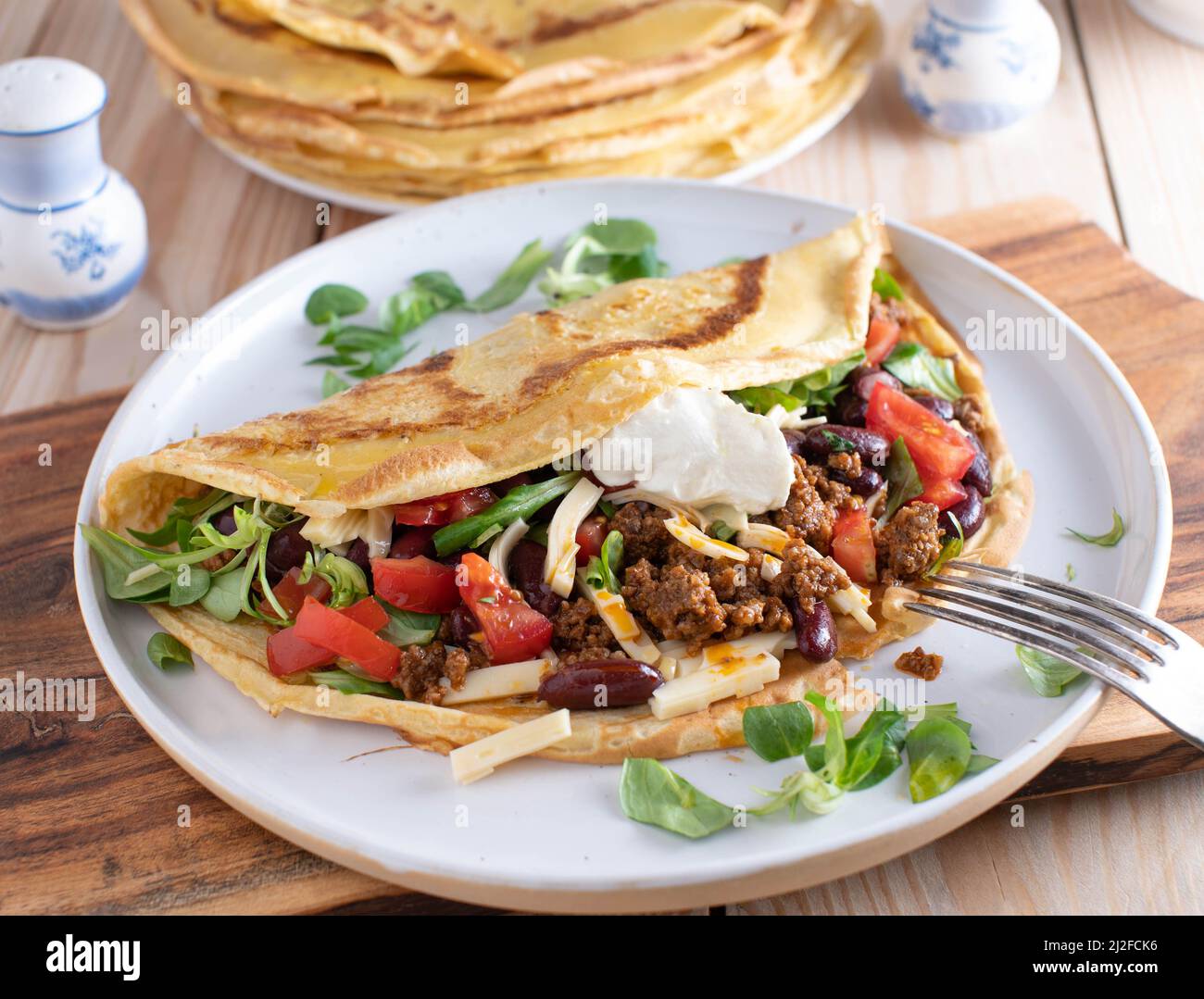 Crêpe savoureuse remplie de bœuf haché épicé, de fromage, de haricots, de laitue et de tomates. Nappés de crème sure et servis sur une assiette. Cuisine Tex mex Banque D'Images