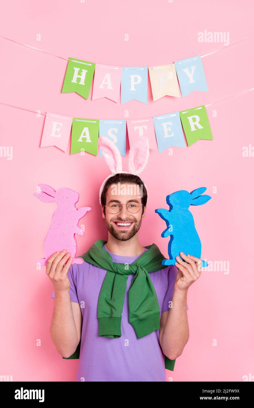 Photo de bonne humeur beau homme mignon célébrer pâques tenir deux petites figurines de lapin isolées sur fond de couleur rose Banque D'Images